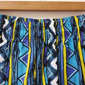May include: Close-up of the waistband of a pair of blue, yellow, white, and purple patterned shorts.