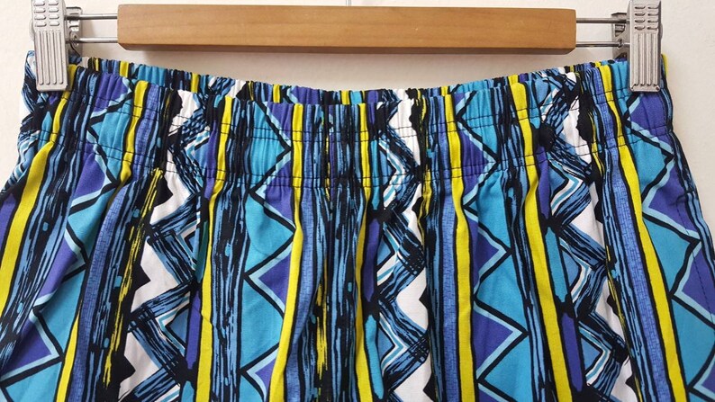 May include: Close-up of the waistband of a pair of blue, yellow, white, and purple patterned shorts.