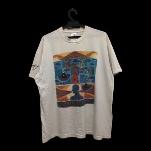 May include: A white t-shirt with a colorful graphic print of a person standing on a scale. The graphic includes a blue sky, a yellow sun, and a red and yellow scale. The text "Libra" is printed below the graphic.