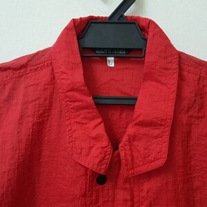 May include: A red long-sleeved shirt with a button-up collar and a single button at the top. The shirt is made of a lightweight, textured fabric.