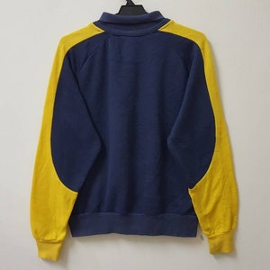 May include: A navy blue sweatshirt with yellow color-blocking on the sleeves. The sweatshirt has a zipper closure and a ribbed collar.