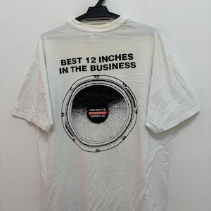 May include: White t-shirt with a black graphic of a speaker and the text "BEST 12 INCHES IN THE BUSINESS". The speaker graphic includes the text "330 WATTS Phase Linear SERIES 48". The shirt is hanging on a black hanger.