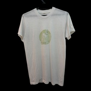 Peut inclure: Un t-shirt blanc à manches courtes avec un motif circulaire sur la poitrine. Le graphique représente un lévrier debout dans un ton vert olive atténué, placé sur un fond circulaire avec des détails de lignes horizontales et du texte sous le chien.
