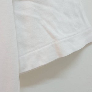 May include: Close-up of the white cotton fabric of a t-shirt sleeve, showing the stitching and hem.
