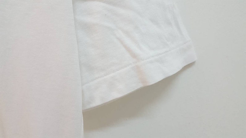 May include: Close-up of the white cotton fabric of a t-shirt sleeve, showing the stitching and hem.
