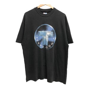 Op de afbeelding: Zwart T-shirt met een cirkelvormige afbeelding van een zilveren "T" met de tekst "TEKNO.COMIX" eromheen.