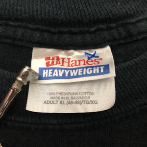 May include: A black Hanes Heavyweight t-shirt tag with white text. The tag says "100% preshrunk cotton, made in El Salvador, Adult XL (46-48)/TG/XG".