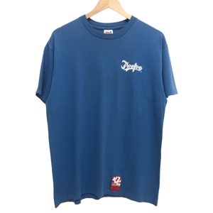 May include: A blue short-sleeved t-shirt with a white "Five Two" logo on the front. The shirt has a red tag on the bottom right corner with the number "12" on it.