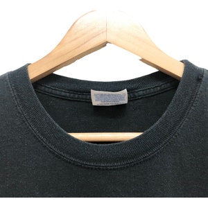 May include: Black t-shirt with a white tag that says "Hanes" on it. The shirt is on a wooden hanger.