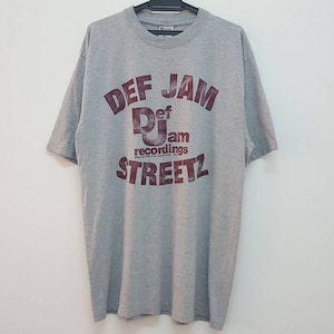 Puede incluir: Camiseta gris con una impresión marrón de "DEF JAM STREETZ" con el logotipo de Def Jam Recordings en el centro.