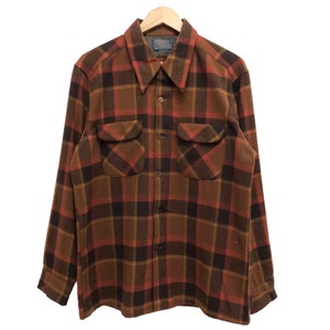 Könnte beinhalten: Ein langärmliges Flanellhemd mit einem braunen, roten und schwarzen Karomuster. Das Hemd hat einen Knopfkragenshirt und zwei Brusttaschen.