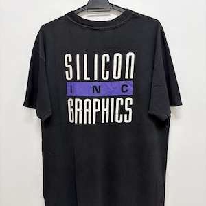 May include: Black t-shirt with the text "SILICON INC GRAPHICS" in white block letters. The word "INC" is on a purple background. The shirt is hanging on a black hanger against a white background.