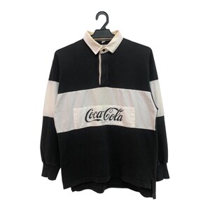 May include: Black and white striped long-sleeve rugby shirt with a Coca-Cola logo on the front.
