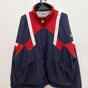 Puede incluir: Chaqueta deportiva Fila vintage en azul marino, rojo y blanco. La chaqueta tiene cremallera completa, cuello alzado y el logo de Fila en el pecho. El diseño incluye detalles en rojo y blanco en hombros y mangas, con dos bolsillos delanteros.