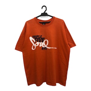 May include: An orange t-shirt with the text "TRIPLE FIVE Soul NYC" in white script. The t-shirt is hanging on a black hanger against a white background. The t-shirt has short sleeves and a crew neck.