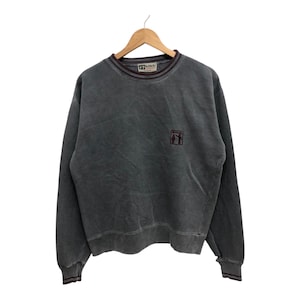 May include: A dark gray sweatshirt with a small embroidered logo on the front. The logo features a stylized image of three people standing together.