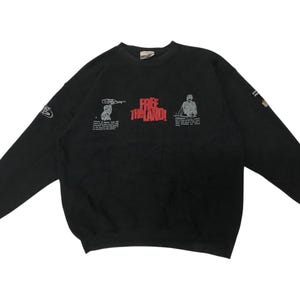 Puede incluir: Sudadera negra de manga larga con un estampado gráfico blanco de dos figuras y el texto "FREE THE LAND".