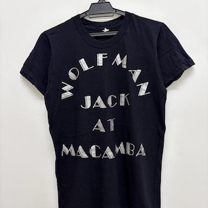 Pode incluir: Uma caneca de cerâmica branca com uma alça preta e o texto "But First, Coffee" em preto, em negrito. A caneca está sobre uma superfície branca.