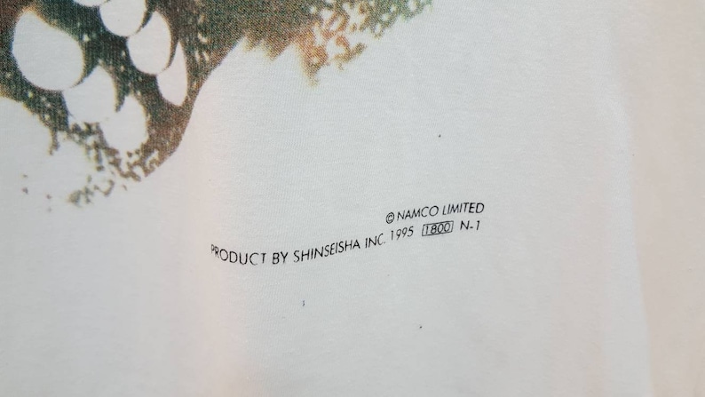 May include: White t-shirt with a green and white graphic print. The text "PRODUCT BY SHINSEISHA INC. 1995 (T800) N.1" and "&copy;NAMCO LIMITED" are printed on the bottom of the shirt.