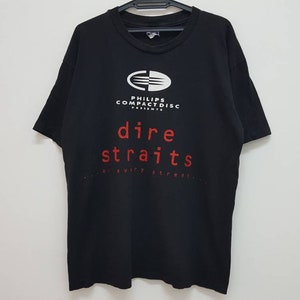 Puede incluir: Camiseta negra con un logotipo blanco que dice "Philips Compact Disc Presents" y un texto rojo que dice "Dire Straits".