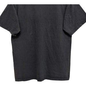 Puede incluir: Una camiseta gris carb&oacute;n con mangas cortas. La prenda tiene un aspecto ligeramente descolorido, lo que sugiere un estilo vintage o desgastado. La tela parece suave y c&oacute;moda, adecuada para ropa informal.