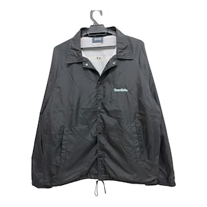 May include: Black coach jacket with a button-up front, collar, and two front pockets. The jacket has the text "Two Sides" in teal on the chest. It is hanging on a black hanger against a white background.