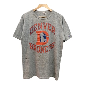 Puede incluir: Una camiseta gris con un logotipo vintage de los Denver Broncos en naranja y azul. El logotipo presenta un caballo y un jinete con las palabras "Denver" y "Broncos" en un diseño circular.
