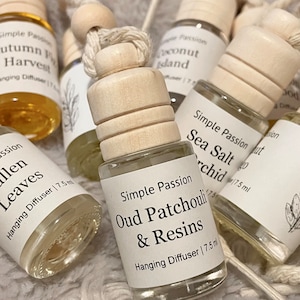 May include: A set of eight small glass bottles with wooden stoppers and string hangers. The bottles are filled with a clear liquid and have labels with the text "Simple Passion" and various scents, including "Autumn Forest Harvest", "Coconut Island", "Sea Salt Orchid", "Fallen Leaves", and "Oud Patchouli & Resins". Each bottle is labeled with "Hanging Diffuser | 7.5 ml".