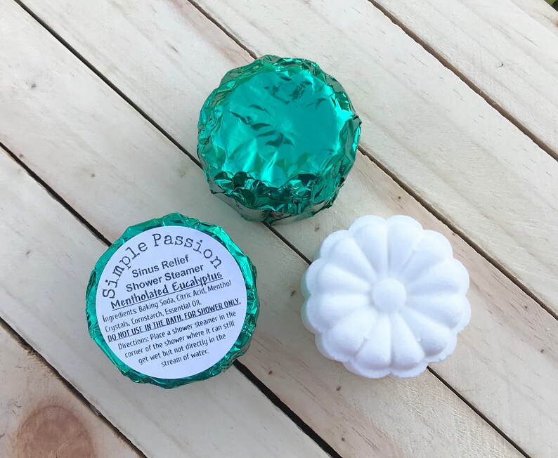 K&ouml;nnte beinhalten: Zwei in gr&uuml;nes Folienpapier verpackte Duschsteamer und ein wei&szlig;er Duschsteamer in Form einer Blume. Die gr&uuml;nen Steamer haben den Text "Simple Passion Sinus Relief Shower Steamer Mentholated Eucalyptus" auf dem Etikett. Das Etikett enth&auml;lt auch Gebrauchsanweisungen: "NICHT IM BAD VERWENDEN, NUR F&Uuml;R DIE DUSCHE. Anleitung: Legen Sie einen Duschsteamer in die Ecke der Dusche, wo er noch nass werden kann, aber nicht direkt im Wasserstrahl."