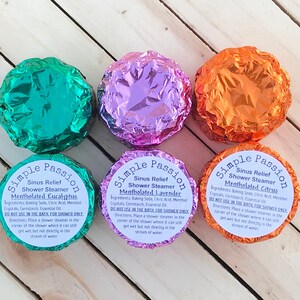 K&ouml;nnte beinhalten: Drei runde Duschdampfer, die in Folie verpackt sind. Die Duschdampfer sind mit "Simple Passion Sinus Relief Shower Steamer" beschriftet und haben die D&uuml;fte "Mentholated Eucalyptus", "Mentholated Lavender" und "Mentholated Citrus".