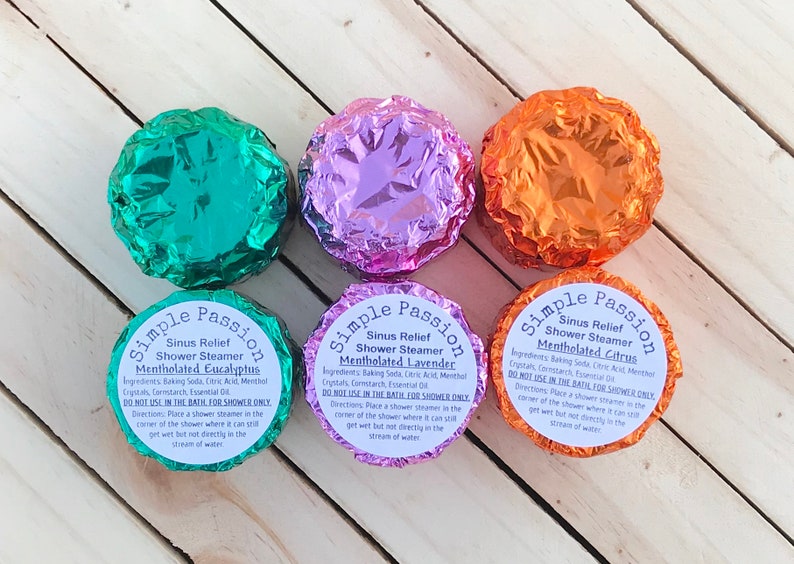 K&ouml;nnte beinhalten: Drei runde Duschdampfer, die in Folie verpackt sind. Die Duschdampfer sind mit "Simple Passion Sinus Relief Shower Steamer" beschriftet und haben die D&uuml;fte "Mentholated Eucalyptus", "Mentholated Lavender" und "Mentholated Citrus".