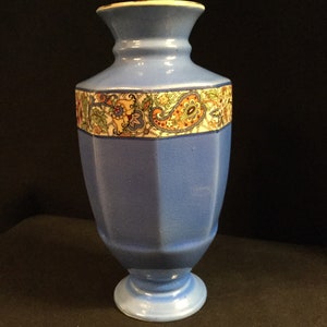 May include: A blue ceramic vase with a geometric design and a floral pattern around the middle. The vase has a wide base and a narrow neck.