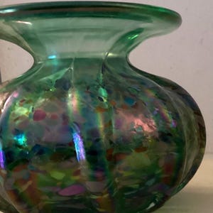 May include: A green glass vase with iridescent speckles and a rounded, bulbous shape.
