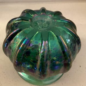May include: A green iridescent glass vase with a bulbous shape and a textured surface. The vase has a wide opening and a small base.