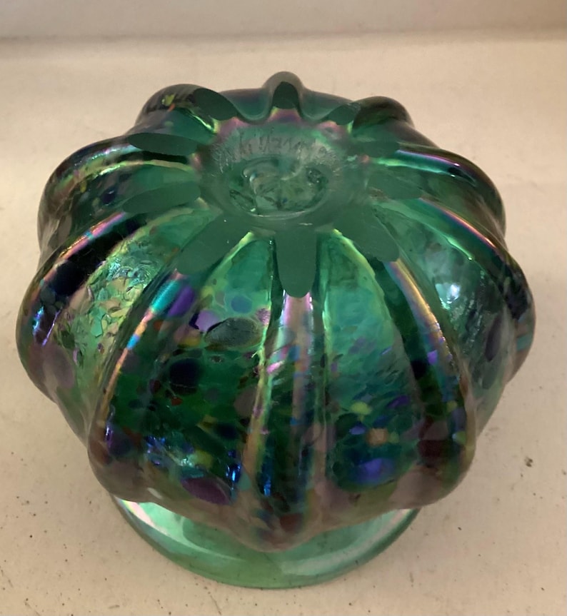May include: A green iridescent glass vase with a bulbous shape and a textured surface. The vase has a wide opening and a small base.