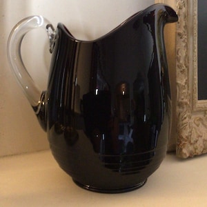 Peut inclure: Un pichet en verre noir avec une poignée en verre transparent. Le pichet a un corps arrondi et un bec large.