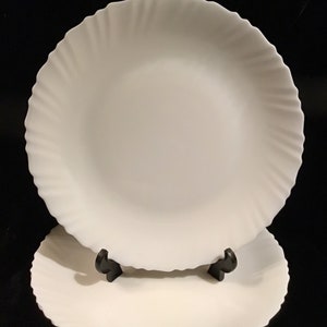 May include: Two white ceramic dinner plates with a scalloped edge. The plates are stacked on top of each other.