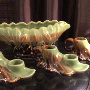 May include: Set of four green and brown ceramic candle holders with a matching green and brown ceramic bowl. The candle holders have a leaf design and the bowl has a scalloped edge.