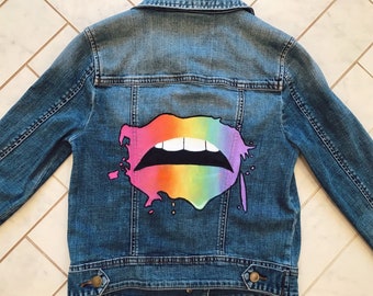Puede incluir: Una chaqueta vaquera azul con un diseño de labios pintados con arcoíris en la espalda.