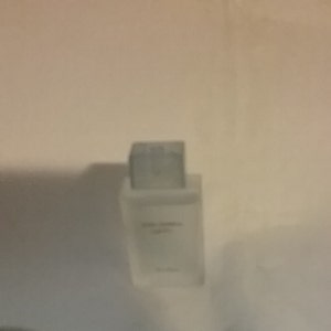 Puede incluir: Un frasco de perfume rectangular de vidrio esmerilado con tap&oacute;n plateado. El frasco tiene un dise&ntilde;o minimalista, con el nombre de la marca y el nombre del producto impresos en una fuente sencilla. El frasco est&aacute; colocado sobre un fondo liso blanquecino.