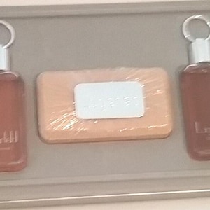 May include: A gift set comprising two brown bottles with silver tops and keyrings, and a bar of soap. The bottles are labelled "Lagerfeld". The soap is wrapped in clear plastic and has a white label.