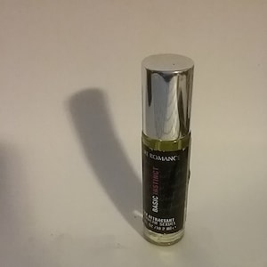 May include: A clear glass roll-on bottle with a silver cap. The label reads "PURE ROMANCE BASIC INSTINCT" with additional text. The bottle contains a light green liquid. The product is 10.2 ml.