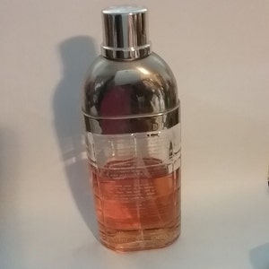 May include: A clear glass perfume bottle with a silver cap and a silver band around the middle. The bottle contains a pink liquid. The bottle is shaped like a cocktail shaker.