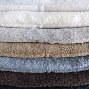 May include: A stack of six fleece blankets in various colours, including white, grey, brown, and black.