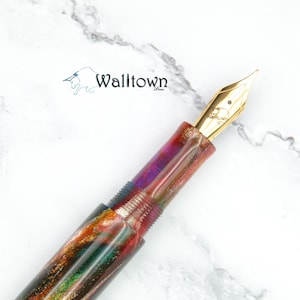 May include: A fountain pen with a gold nib and a multi-coloured body. The pen's body has a swirling pattern of red, green, purple, and gold. The pen is set against a white marble background. The brand name "Walltown" is visible.