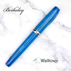 May include: A blue pen with silver accents, set against a white marble background. The pen has a sleek design and the word "Berkeley" is written in cursive at the top. The Walltown logo is at the bottom.