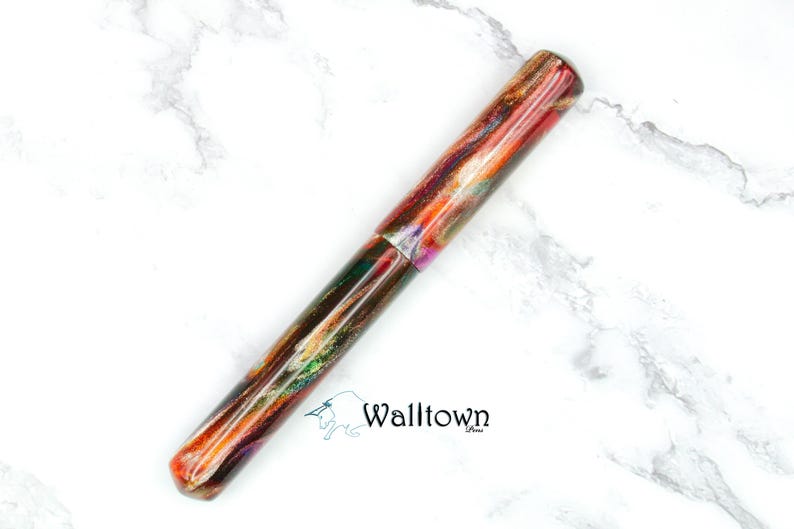May include: A colourful pen with a marbled design in shades of red, orange, green, and purple. The pen has a rounded tip and a cap. The pen is lying on a white marble surface. The word "Walltown" is printed on the surface.