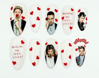 May include: Set of white nail art with images of men holding roses, red heart accents, and the text "Would he say he's in L-O-V-E?" on some nails. The nails are almond-shaped.