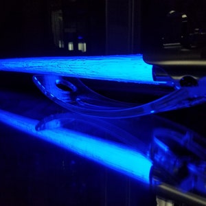 May include: A blue lightsaber on a clear plastic stand. The lightsaber is lit and glowing.