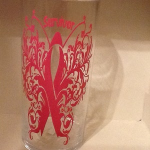 May include: A clear glass tumbler with a pink butterfly design and the word "Survivor" printed on the front.